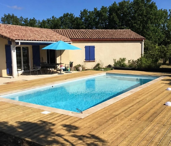 Piscine maçonnée réalisée par Bati-System avec terrasse en bois devant une maison